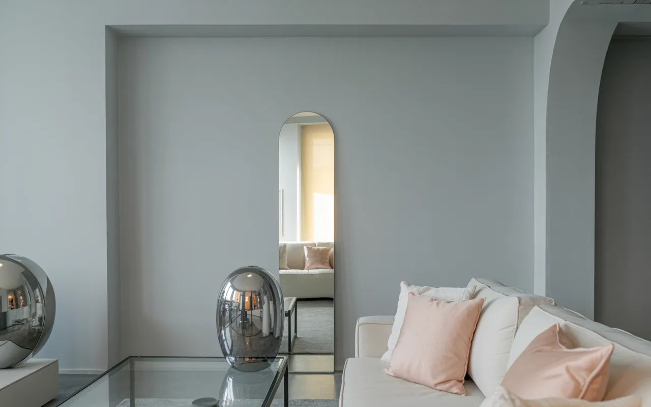 Small living room with light grey walls, pink cushions, mirrored décor, and minimal furniture