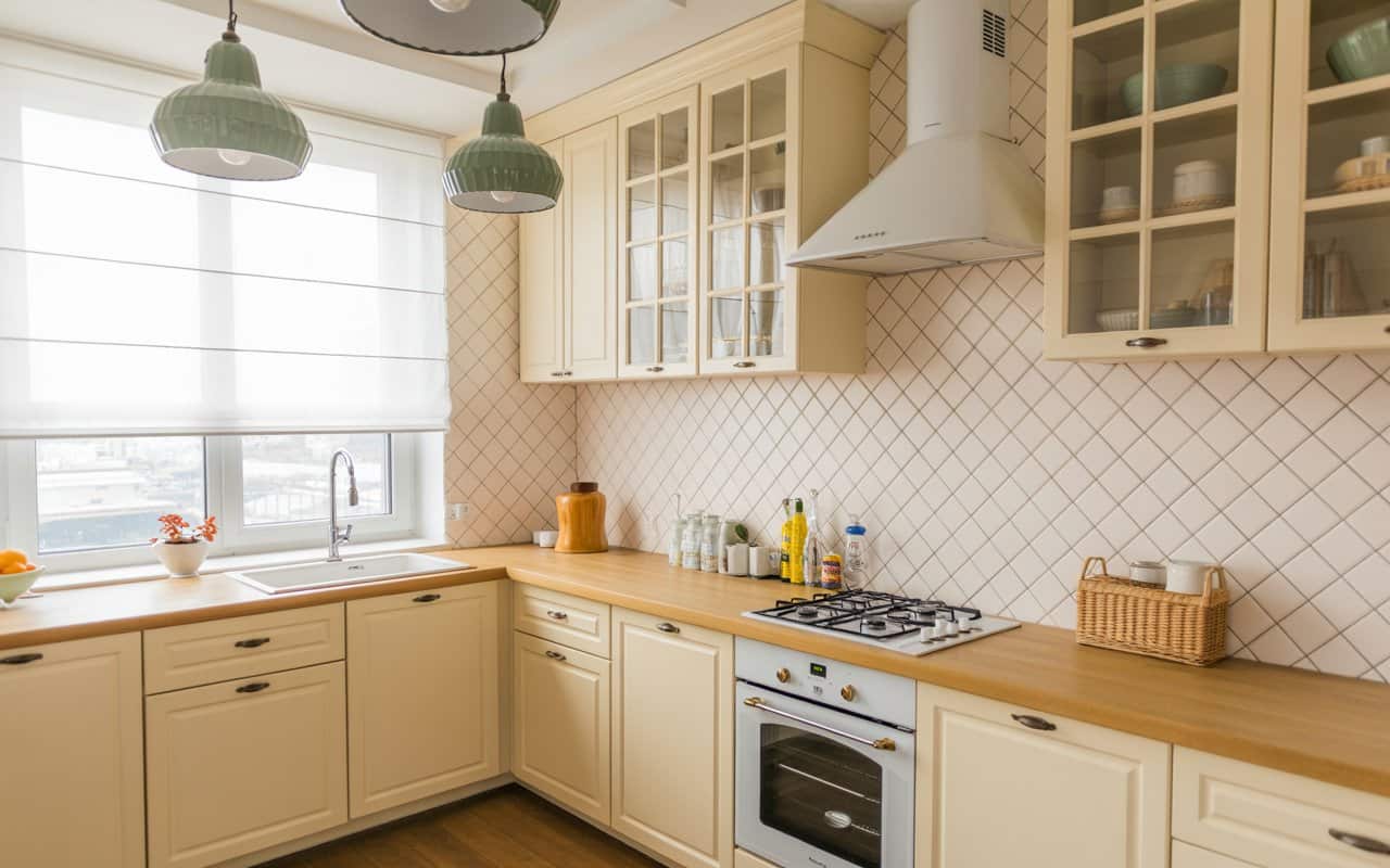 Bright kitchen with geometric tile backsplash, white cabinets, wooden countertop, stylish pendant lights, cozy and modern vibe
