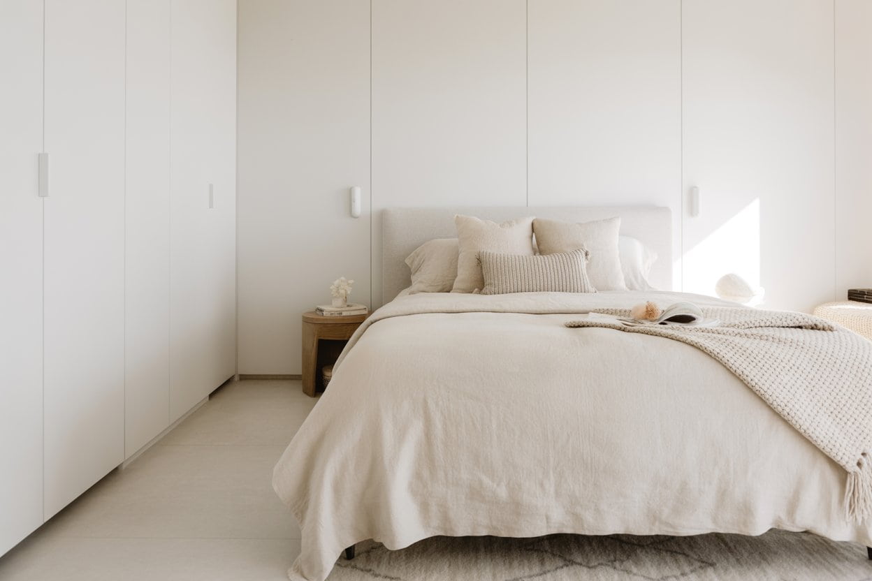 White minimalist bedroom with layered textures, knitted throw, soft linen bedding, wooden bedside table, cozy elegant interior, Pinterest aesthetic.”
