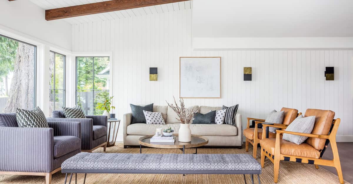 “Small living room with concrete floor, seating area with dark beige sofa, layered rug, wooden side table, modern décor”