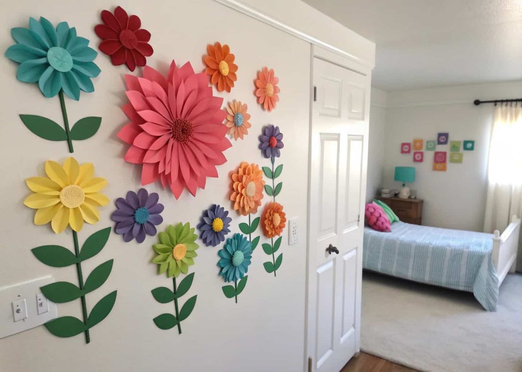 Colorful paper flowers arranged on a white bedroom wall creating a bright decorative display