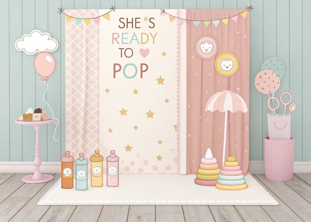 A pastel-colored baby shower photo booth with a “She’s Ready to Pop” backdrop and props like baby bottles, pacifiers, and tiny hats, with happy guests taking photos.
