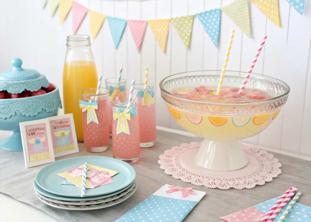 A pastel baby shower drink station with colorful punch, decorated glasses, cute straws, and tags, on a decorated table.
