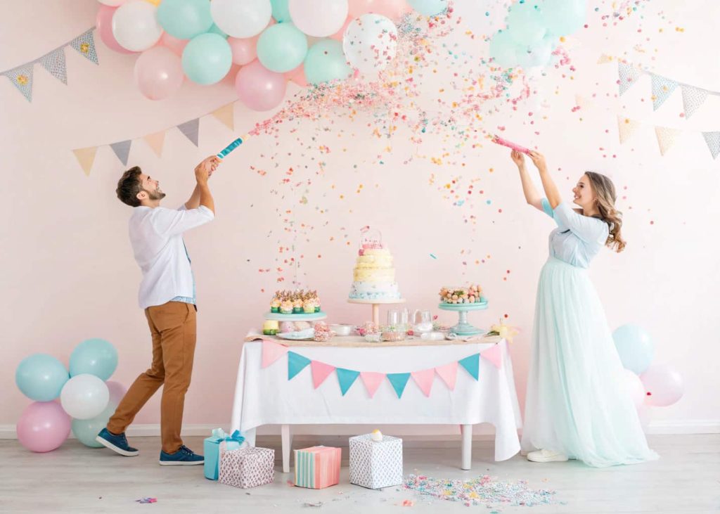 “Guests at a pastel baby shower using confetti poppers, colorful confetti flying, with a decorated table and balloons in the background.”