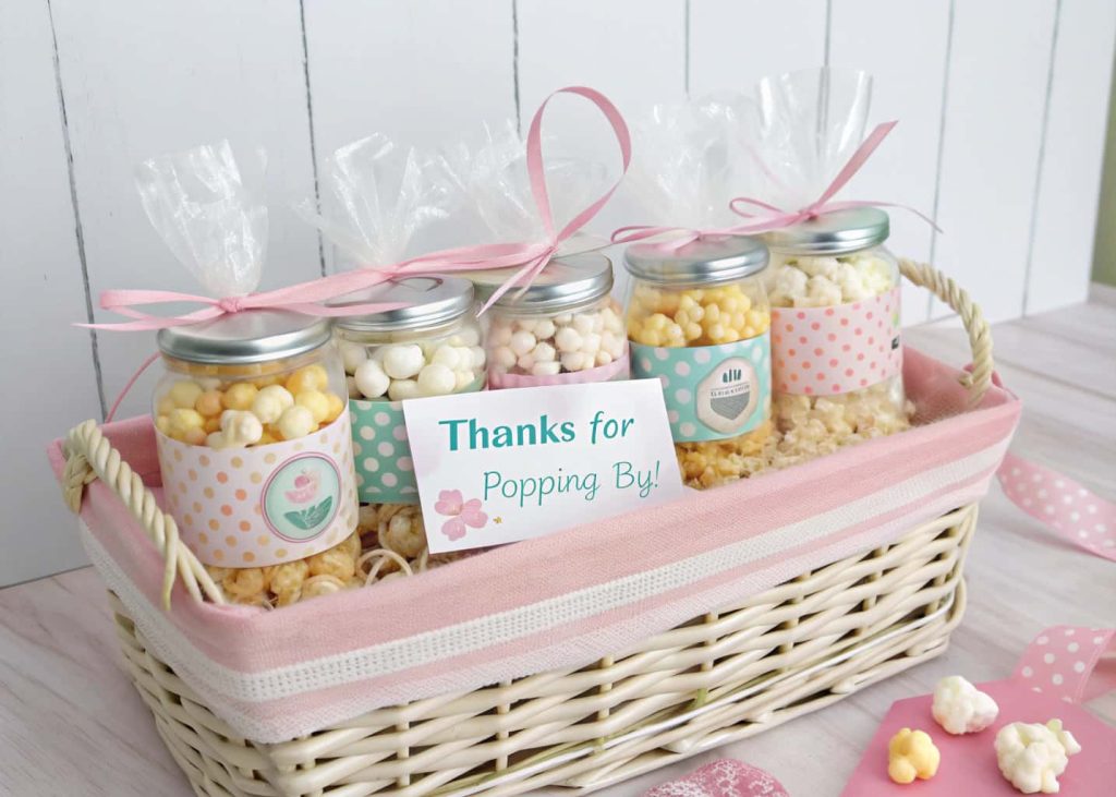 A pastel basket with personalized baby shower favors including mini popcorn jars, candy bags, and ‘Thanks for Popping By!’ tags.”
