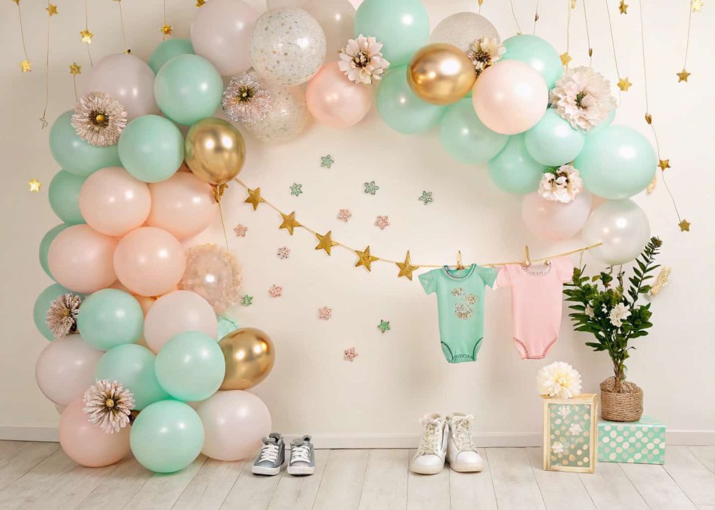 A pastel and metallic balloon garland backdrop decorated with small flowers and baby-themed items for a baby shower photo area.”