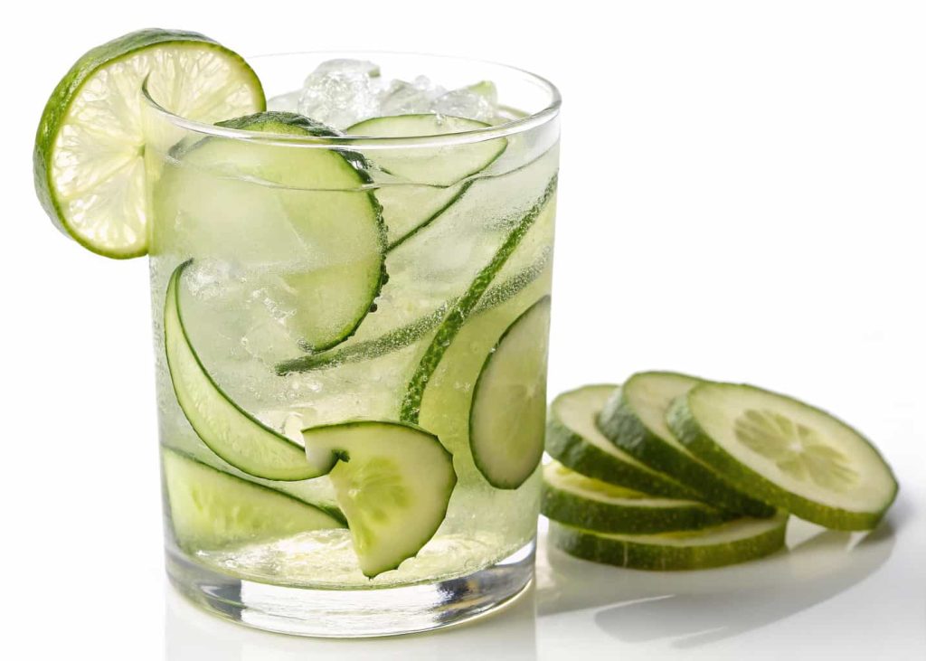 A cucumber lime mocktail with thin cucumber slices and ice in a clear glass