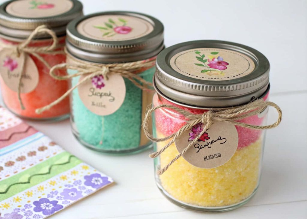 Colorful homemade bath salts in small jars with twine and labels for party favors.”