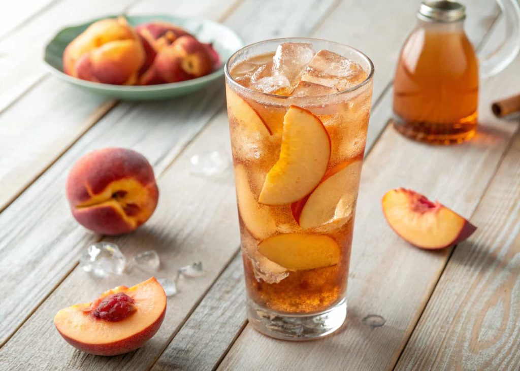 A peach iced tea mocktail with peach slices and ice cubes in a tall glass, soft summer lighting