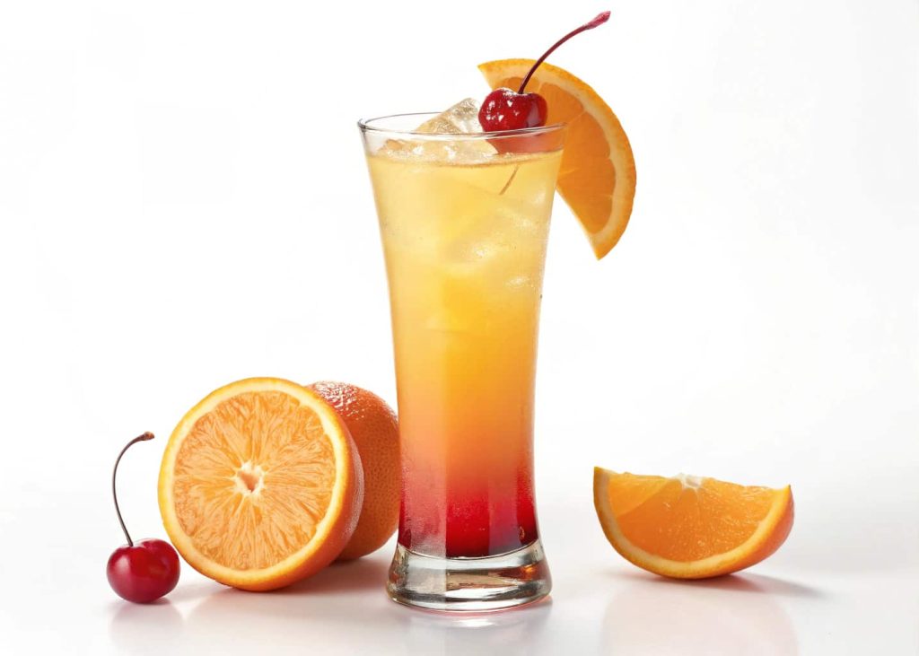An orange sunrise mocktail with layered colors, orange slice, and cherry garnish in a tall glass