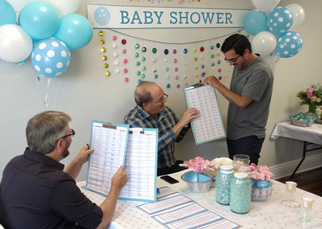 Guests participating in a baby shower quiz with score sheets and prizes on a decorated table”