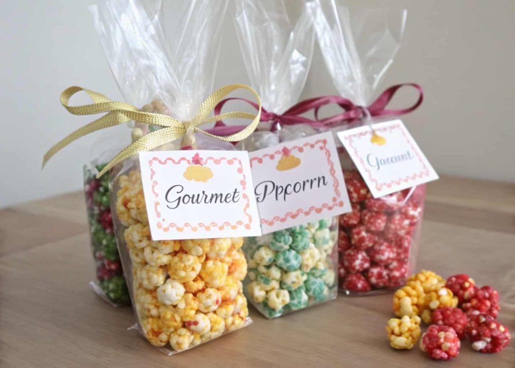 Clear bags of colorful gourmet popcorn tied with ribbons and personalized tags for party favors.”