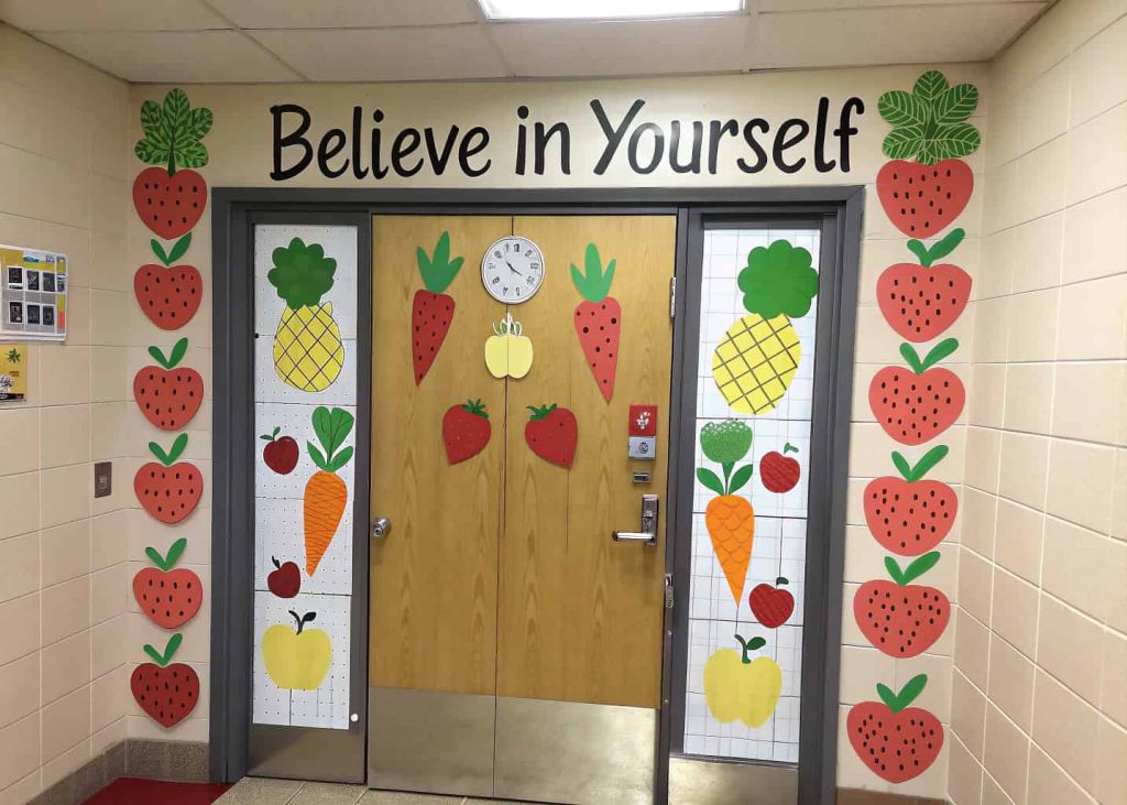 Door decorated with colorful paper fruits and vegetables and a motivational classroom sign.
