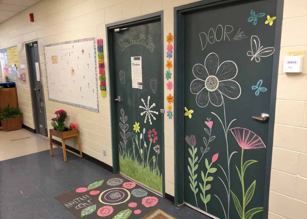 Classroom door covered in chalkboard paper with spring-themed drawings and space for student messages.