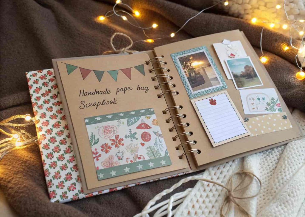 Handmade paper bag scrapbook with decorated pages, photo pockets, and handwritten notes resting on a cozy blanket.
