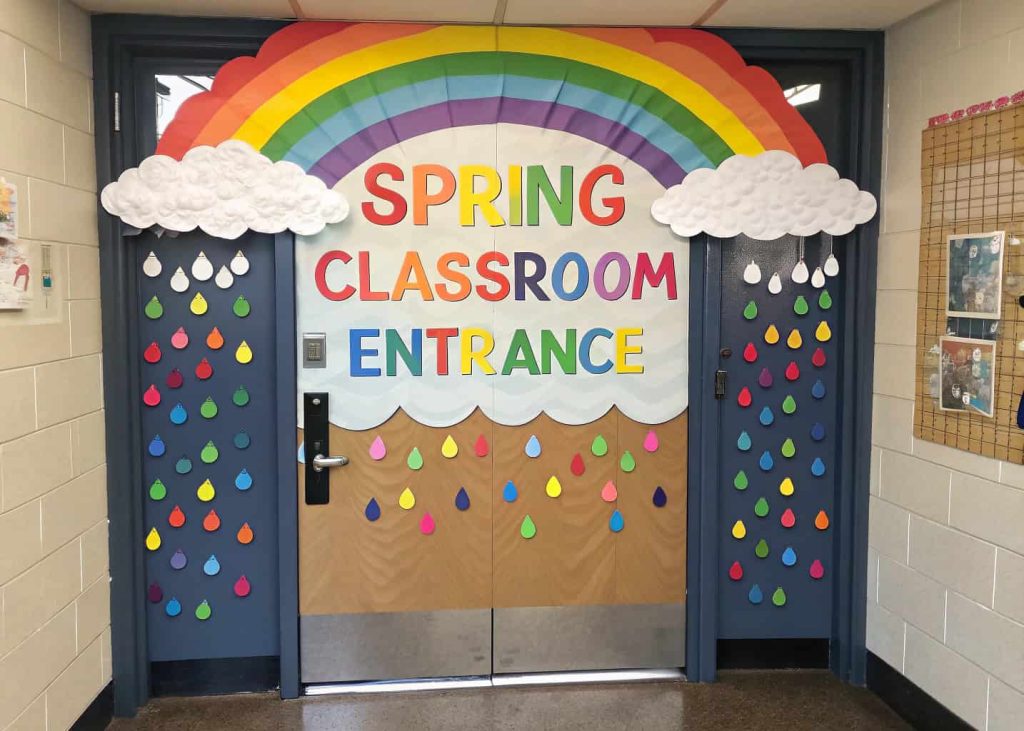 Door with a large paper rainbow and fluffy white clouds, positive words on colorful raindrops, cheerful spring classroom entrance.