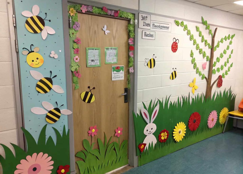 Classroom door decorated with paper bees, ladybugs, and bunnies among colorful flowers and grass, playful spring garden theme.