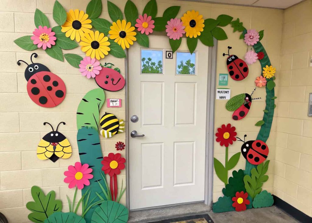 Door decorated with colorful paper insects like caterpillars, ladybugs, and bees, flowers and leaves around, fun spring theme.