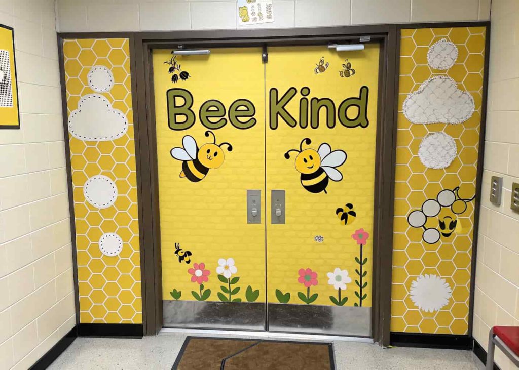 classroom door with bee theme, honeycomb shapes, “Bee Kind” text, cute bees and bright yellow colors