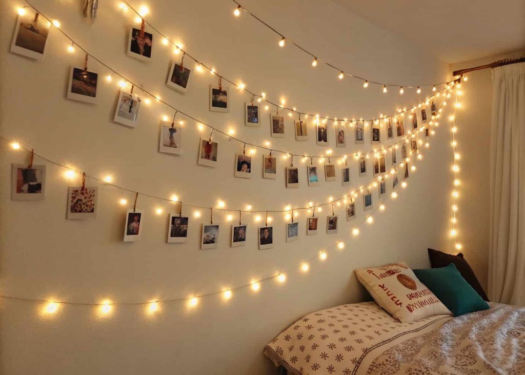 Bedroom wall decorated with warm white string lights and clipped photos.