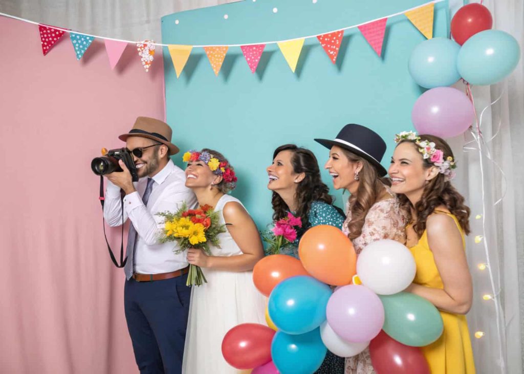 Wedding photo booth with themed props, colorful backdrop, and guests taking pictures.