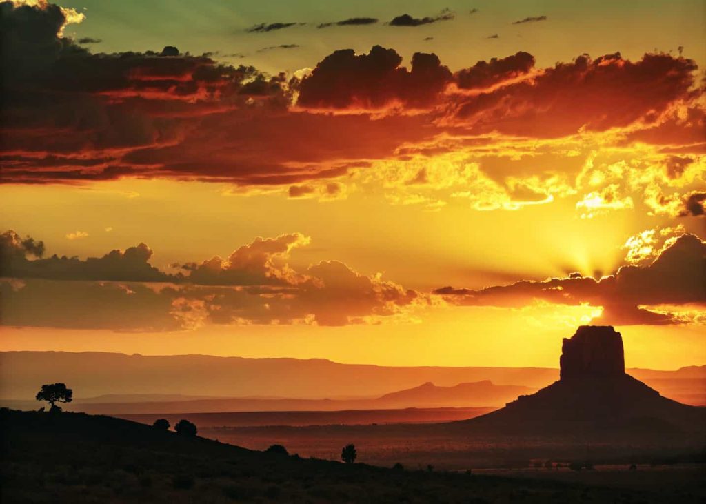 Golden hour sunset sky with vivid red-orange-yellow gradient fading into soft lemon green, dramatic cloudscape, warm cinematic photography, silhouette of landscape against glowing sky, travel and adventure editorial mood, rich saturated colors, wide panoramic composition.