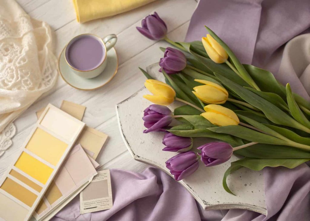 Lilac purple and butter yellow spring color palette, vintage aesthetic flat lay with spring tulips, pastel fabric swatches, soft bokeh background, nostalgic spring morning light