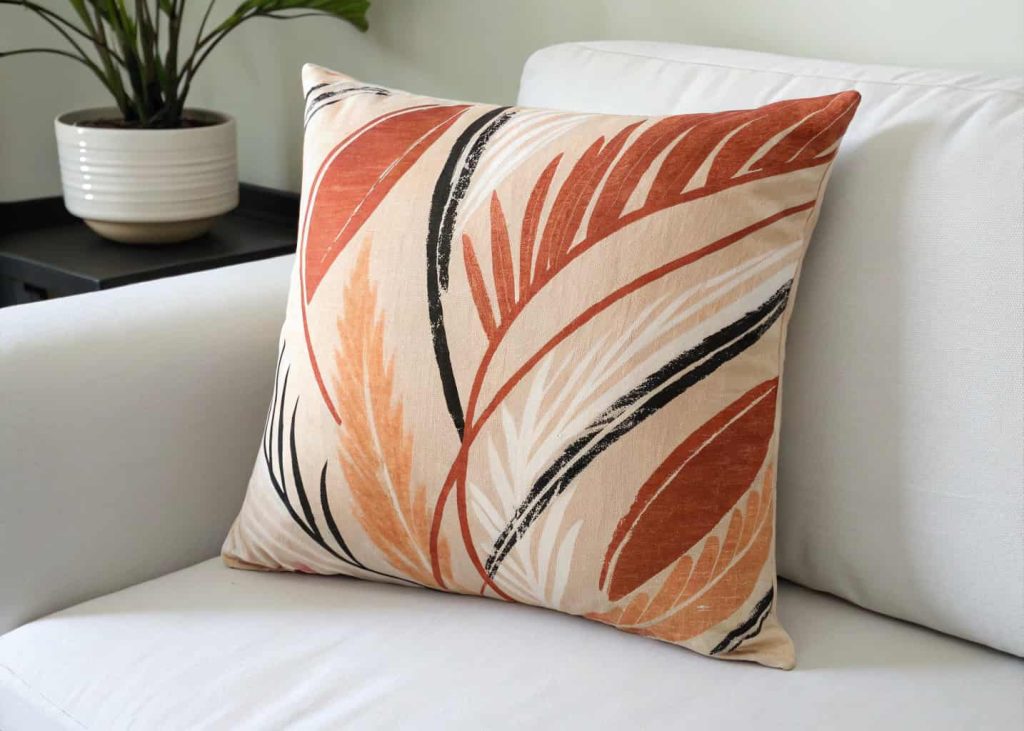 Hand-painted abstract color block pillow cover in warm terracotta, cream, and black brushstrokes on cotton fabric, styled on a minimalist white sofa