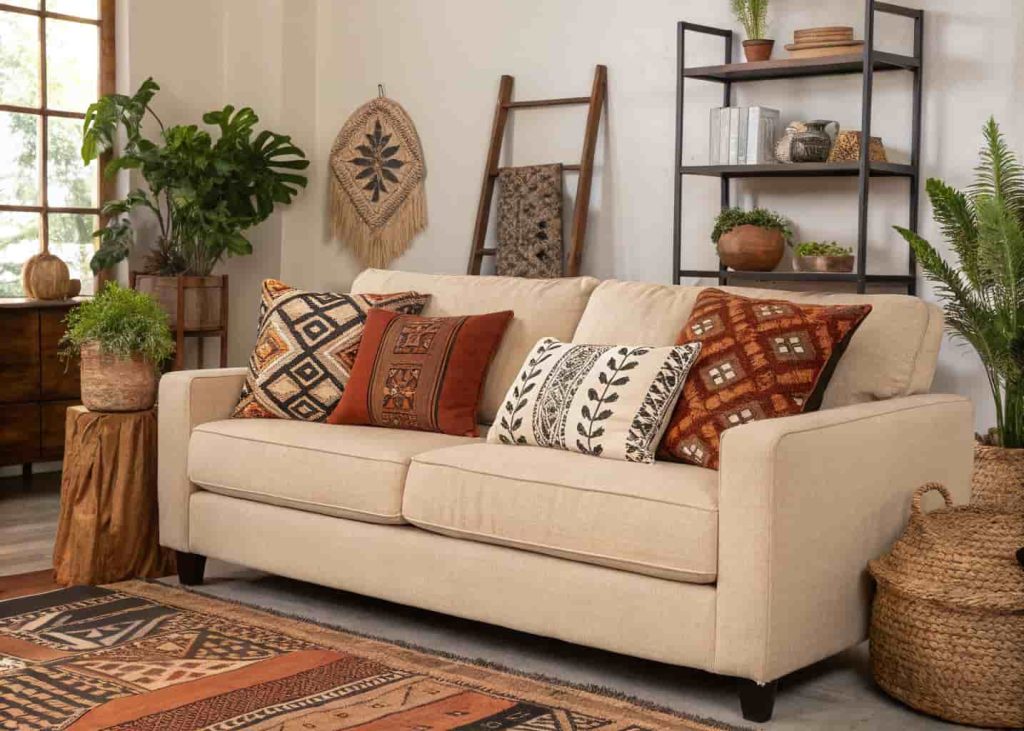 A tan linen sofa with global-inspired throw pillows featuring block print and mud cloth patterns in rust, black, and cream, bohemian modern living room with plants and wooden accents, interior photography