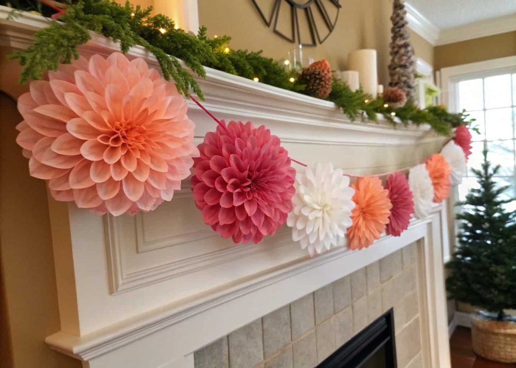 A colorful tissue paper flower garland in pink, coral, and white, strung across a fireplace mantel with greenery, warm home interior, festive and cozy atmosphere, lifestyle photography.