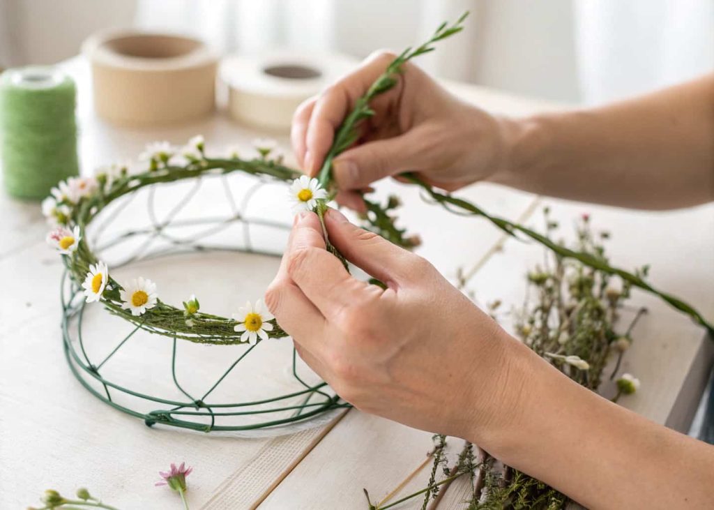 Hands wrapping green floral tape around small flowers on a wire crown base, step-by-step craft process, close-up detail shot, soft background lighting.