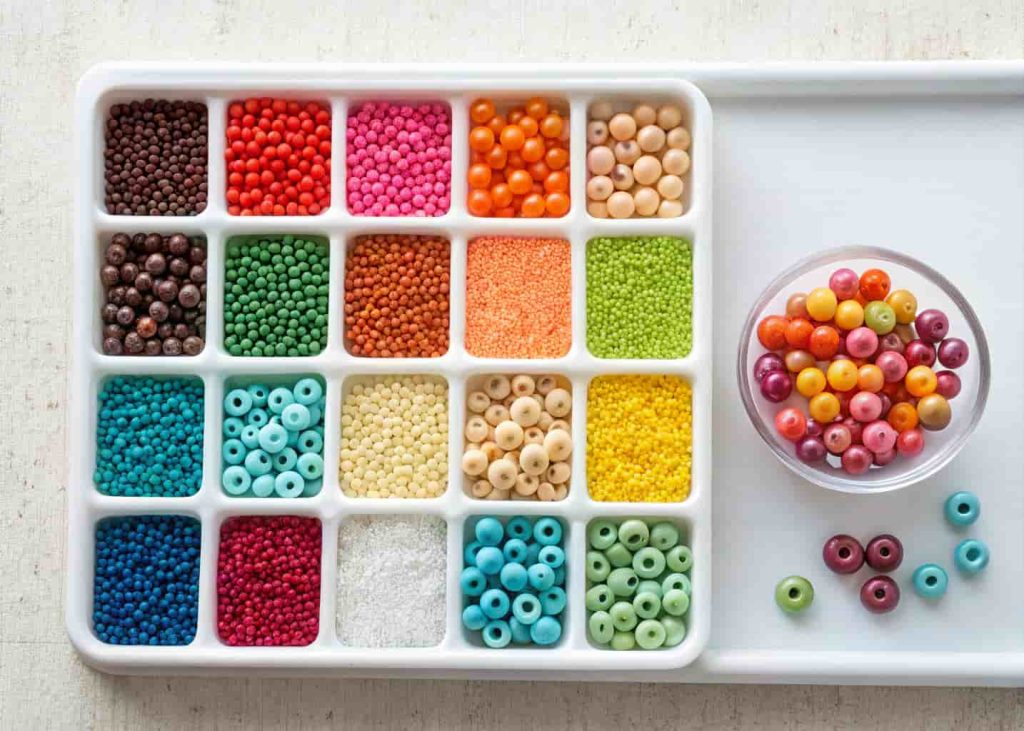 A flat lay of colorful seed beads sorted by color and size on a white tray, natural lighting, craft photography style.