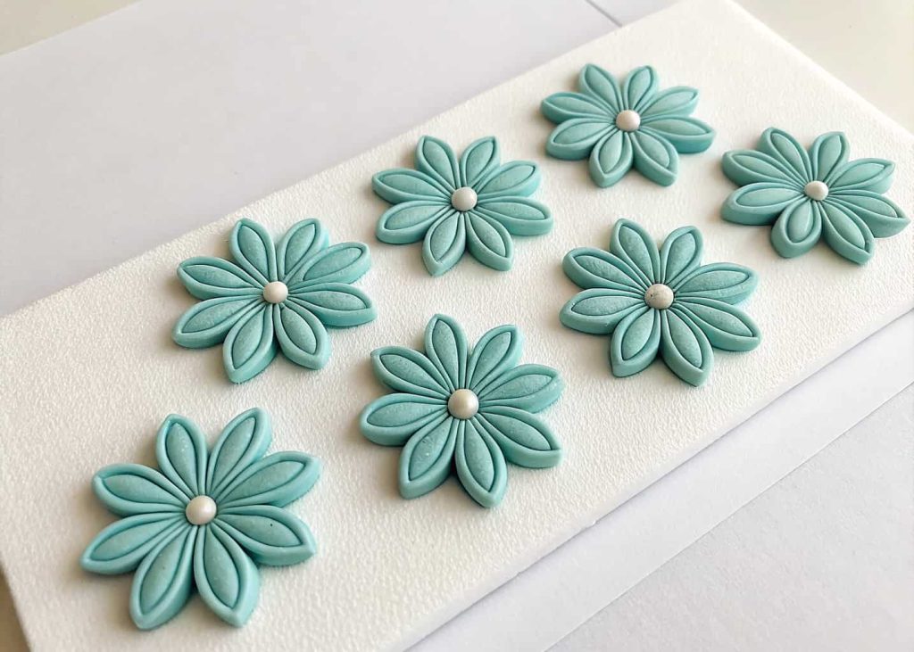 Six matching bead flower petals laid out in a row on a white foam board, same color beads, top-down flat lay craft photo.
