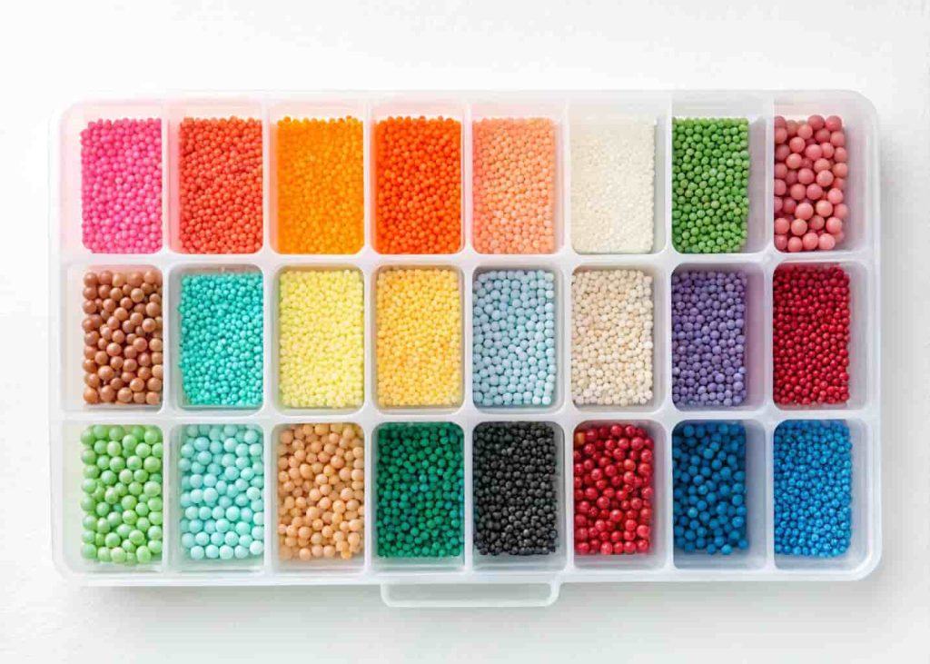 Bead organizer tray with small compartments each filled with different colored seed beads, top-down view, clean white background.