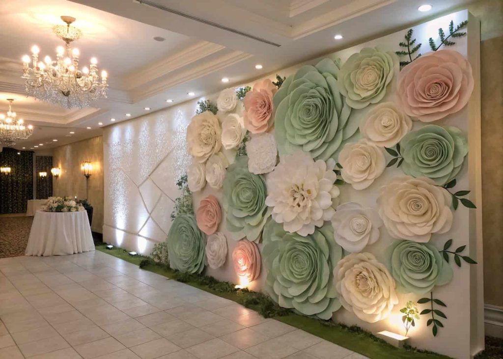 A breathtaking giant paper flower wall backdrop in shades of white, blush, and sage green at a wedding reception, soft romantic lighting, elegant and luxurious event design, wide angle shot showing full installation on wall.