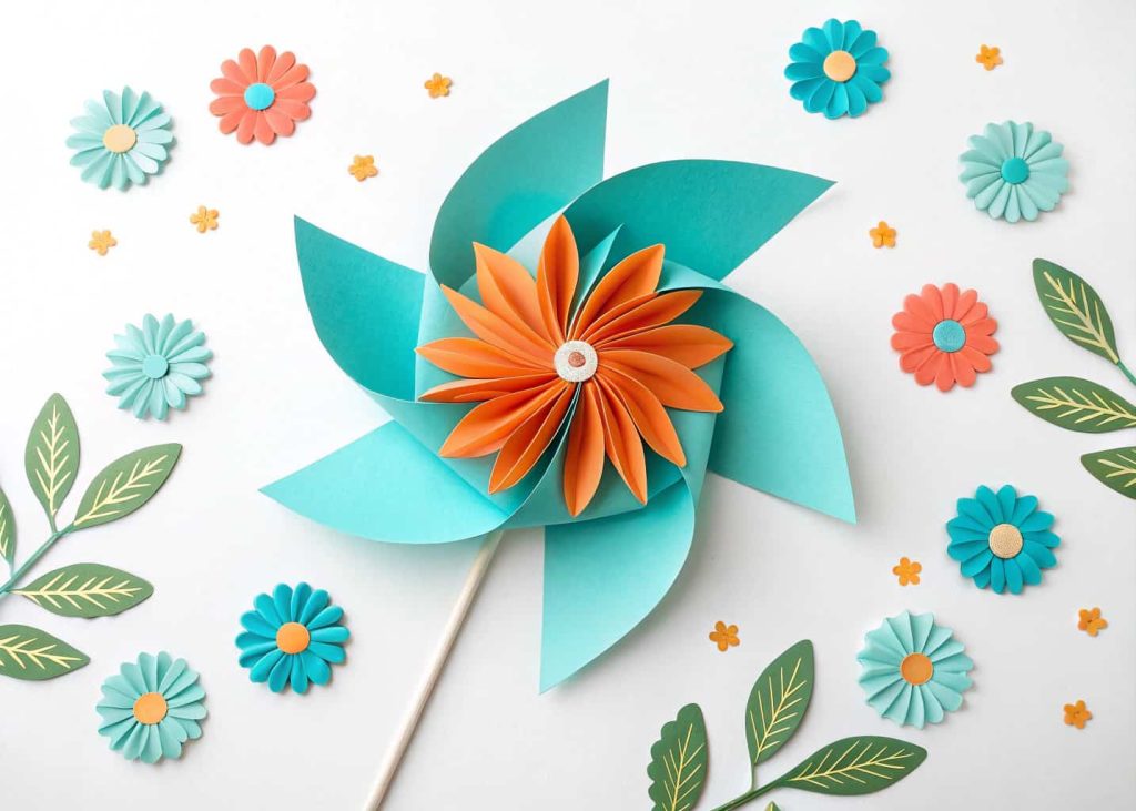 A vibrant pinwheel paper flower in turquoise and orange layers on a white background, flat lay, graphic and playful style, bright studio lighting, top-down view, clean and joyful composition.