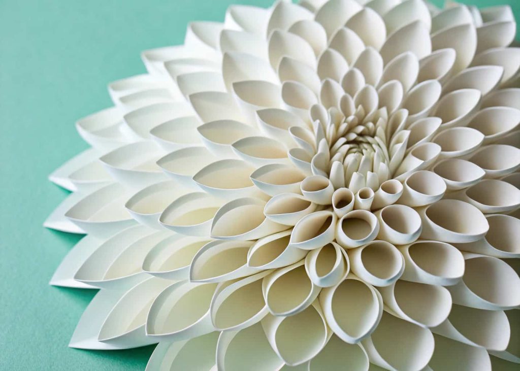 A full and detailed paper dahlia made from looped white paper strips, multiple layered rings of petals visible, centered on a soft mint green background, macro detail shot, bright and clean lighting, impressive handmade craft result.