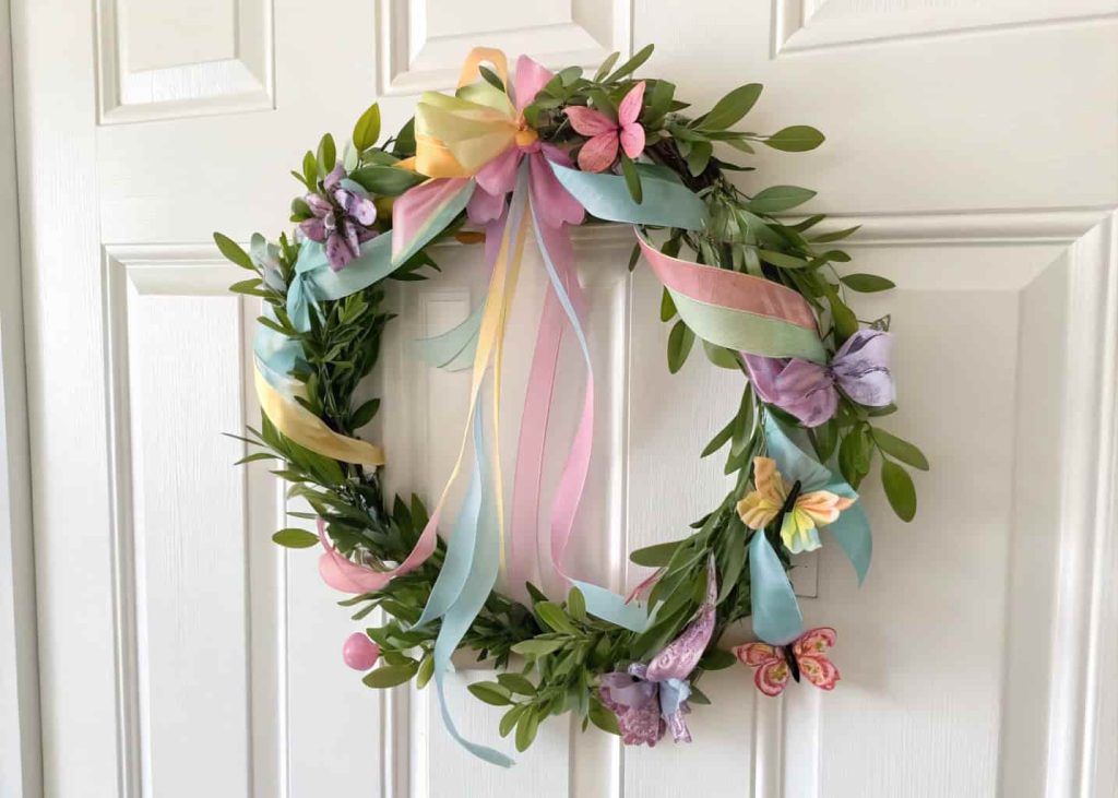 A wreath with pastel ribbons, small butterflies, and green leaves on a white door.