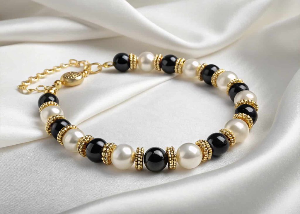 Elegant faux pearl and black bead bracelet with gold clasp on white satin