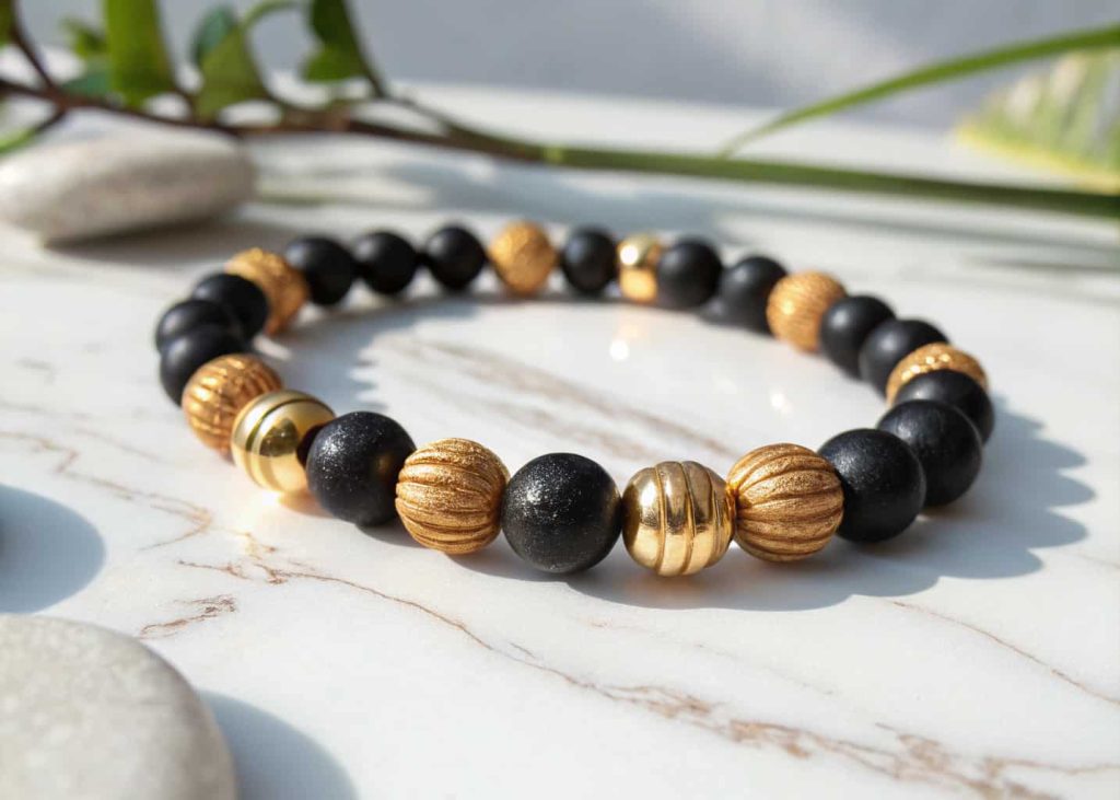 A handmade bracelet with alternating matte black and gold shiny beads placed on a white marble surface with soft natural lighting
