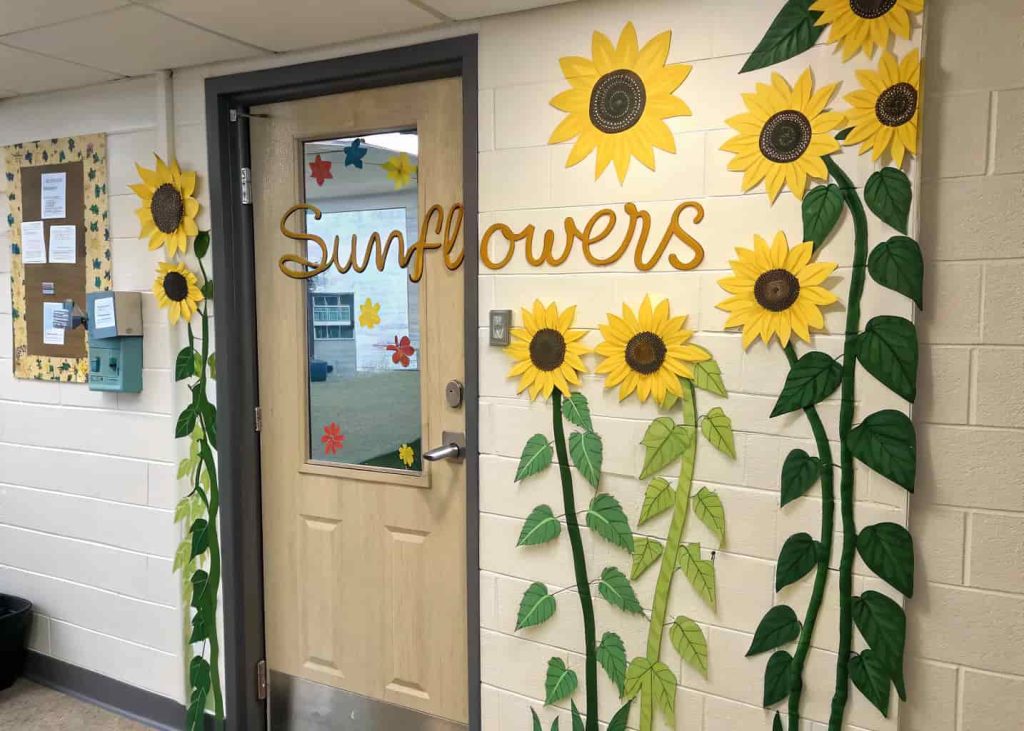Classroom door decorated with large sunflowers, green stems, leaves, and a welcoming message.