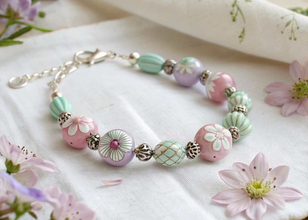 Pastel floral lampwork glass bead bracelet on white linen with scattered flower petals