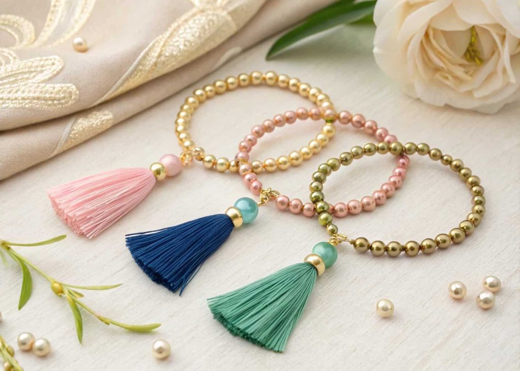 Three gold bead bracelets with silk tassels in pink blue and green on cream textured background