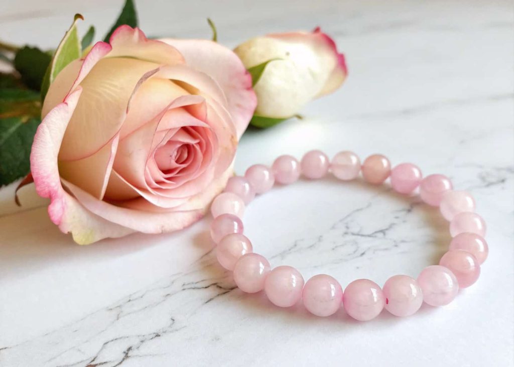 Rose quartz bead bracelet on white marble surface next to a single dried rose