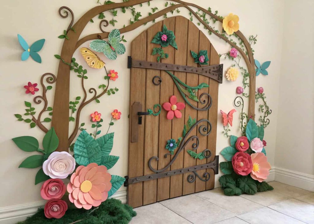 Door designed as a wooden garden gate surrounded by paper flowers, butterflies, and vines.