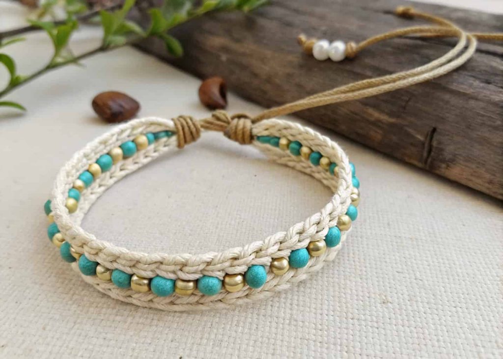 Cream macramé wrap bead bracelet with turquoise and brass beads worn wrapped around a wrist on linen