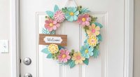 A bright, floral spring door hanger on a white front door with pastel-colored flowers and a small welcome sign.
