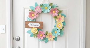 A bright, floral spring door hanger on a white front door with pastel-colored flowers and a small welcome sign.
