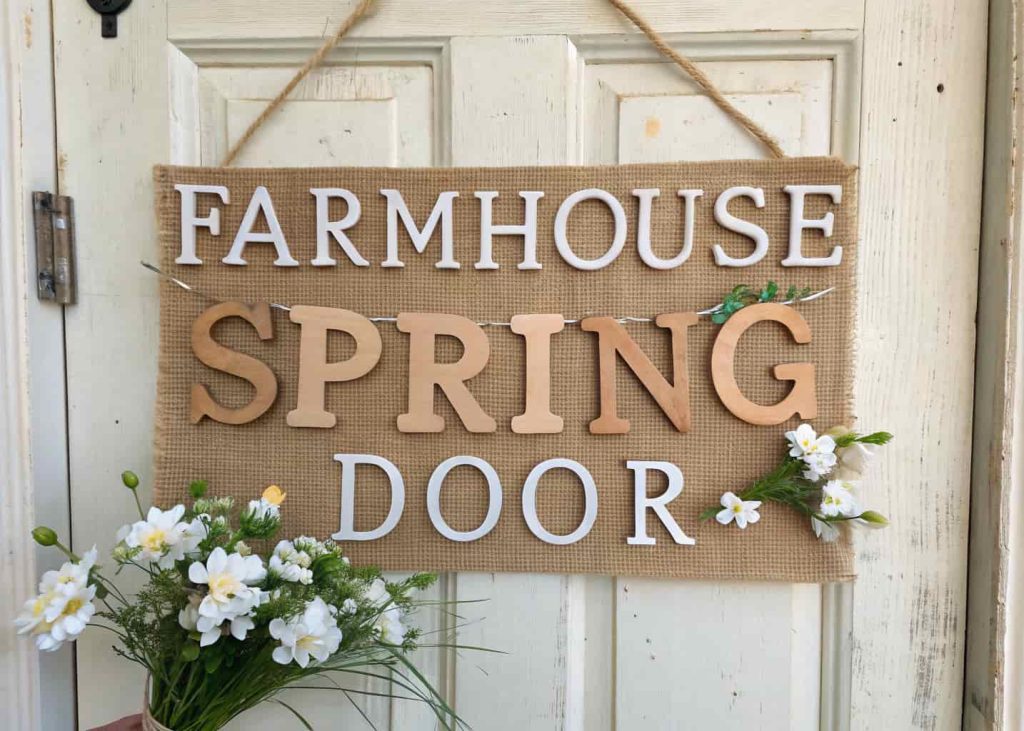 Rustic farmhouse spring door hanger with burlap, wooden letters, and white flowers on a farmhouse-style door.