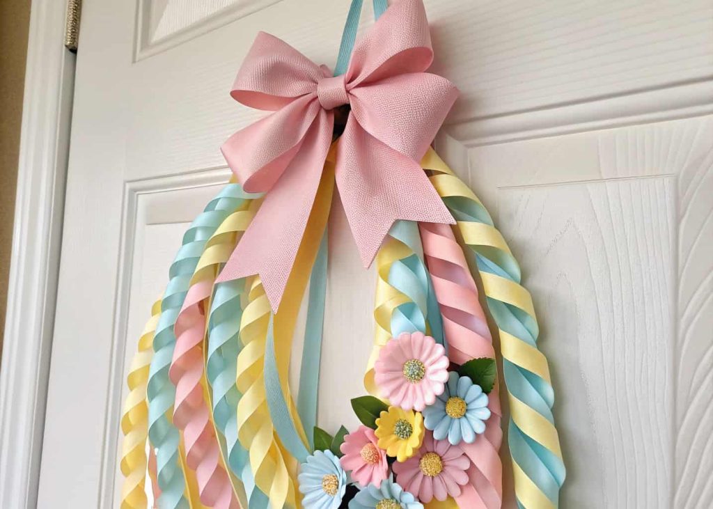 Spring door hanger with layered pastel ribbons, a bow at the top, and small artificial flowers attached.